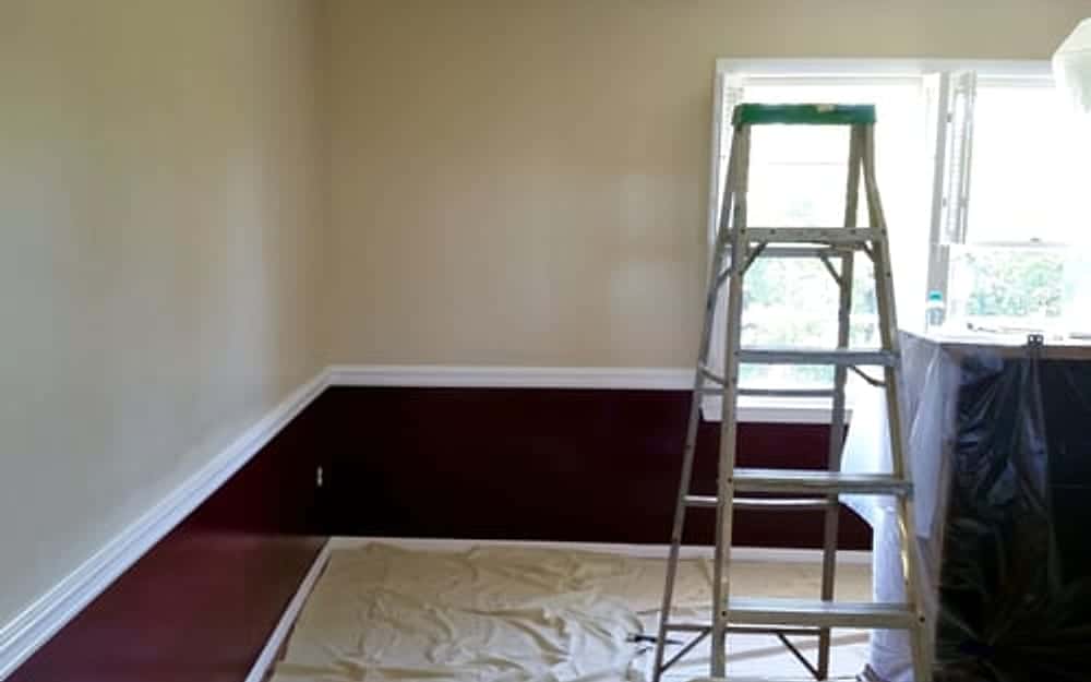 Empty room with a ladder and protected flooring prepared for interior painting